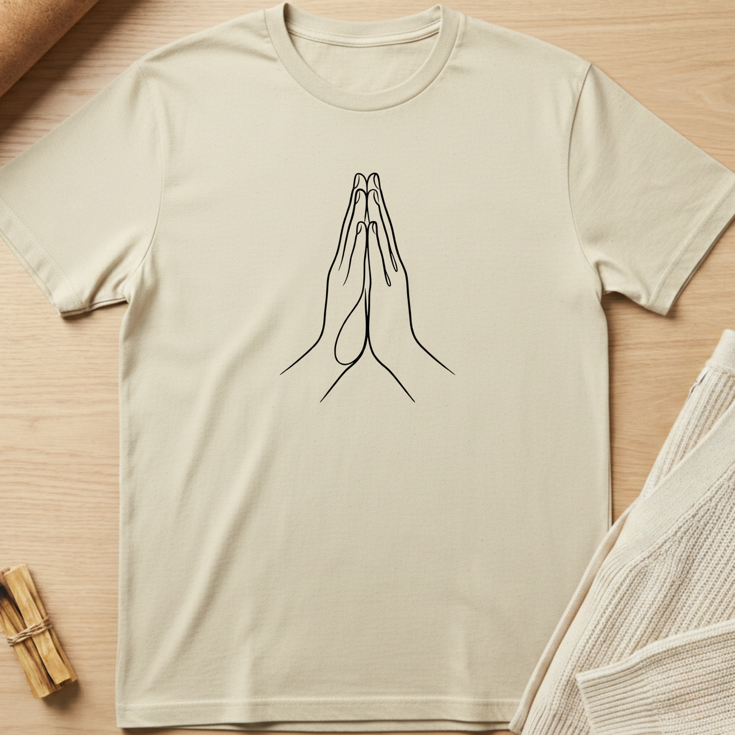Beige t-shirt with a line drawing of praying hands on a wooden surface. Minimalist yoga apparel by pemuyo.