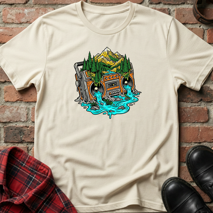 Beige t-shirt with a graphic design of a vintage radio in a forest, placed against a brick wall. Minimalist music apparel by pemuyo.