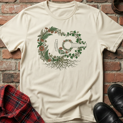 Beige t-shirt with a guitar and floral design on a brick background. Minimalist music apparel by pemuyo.