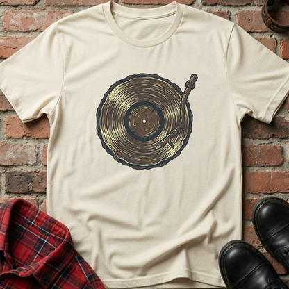 Beige t-shirt with a graphic design of a vinyl record and needle on a brick wall background. Minimalist music apparel by pemuyo.
