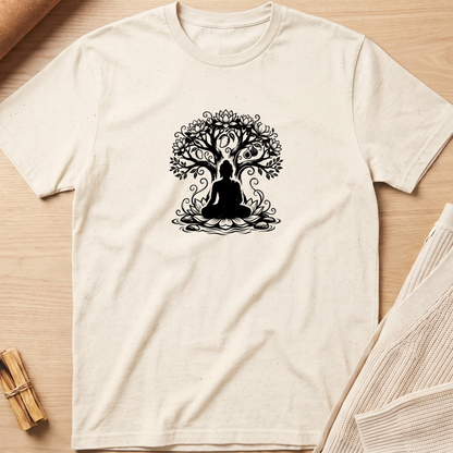 An off-white short-sleeve t-shirt with a black graphic of a meditating figure inside a tree, laid flat on a light wood background with styled props. Minimalist yoga apparel by pemuyo.