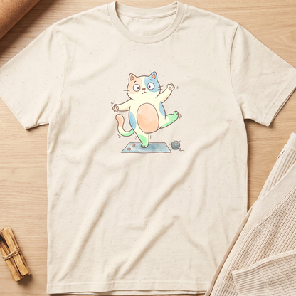 An off-white short-sleeve t-shirt with a colorful cartoon cat graphic, laid flat on a light wood background with a knit fabric prop in the corner. Minimalist yoga apparel by pemuyo.