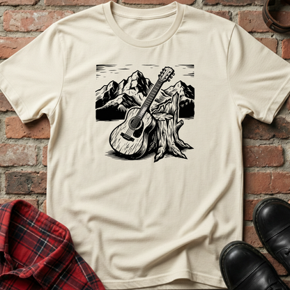 Beige t-shirt with a guitar and mountain graphic on a brick wall background. Minimalist music apparel by pemuyo.