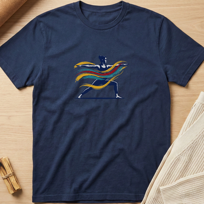 A navy blue short-sleeve t-shirt laid flat on a light wood surface, featuring a colorful graphic of a warrior silhouette with flowing yellow, orange, and red stripes. Styled flat-lay props include a rolled tan material in the top-left and a folded cream knit fabric in the bottom-right. Minimalist yoga apparel by pemuyo.