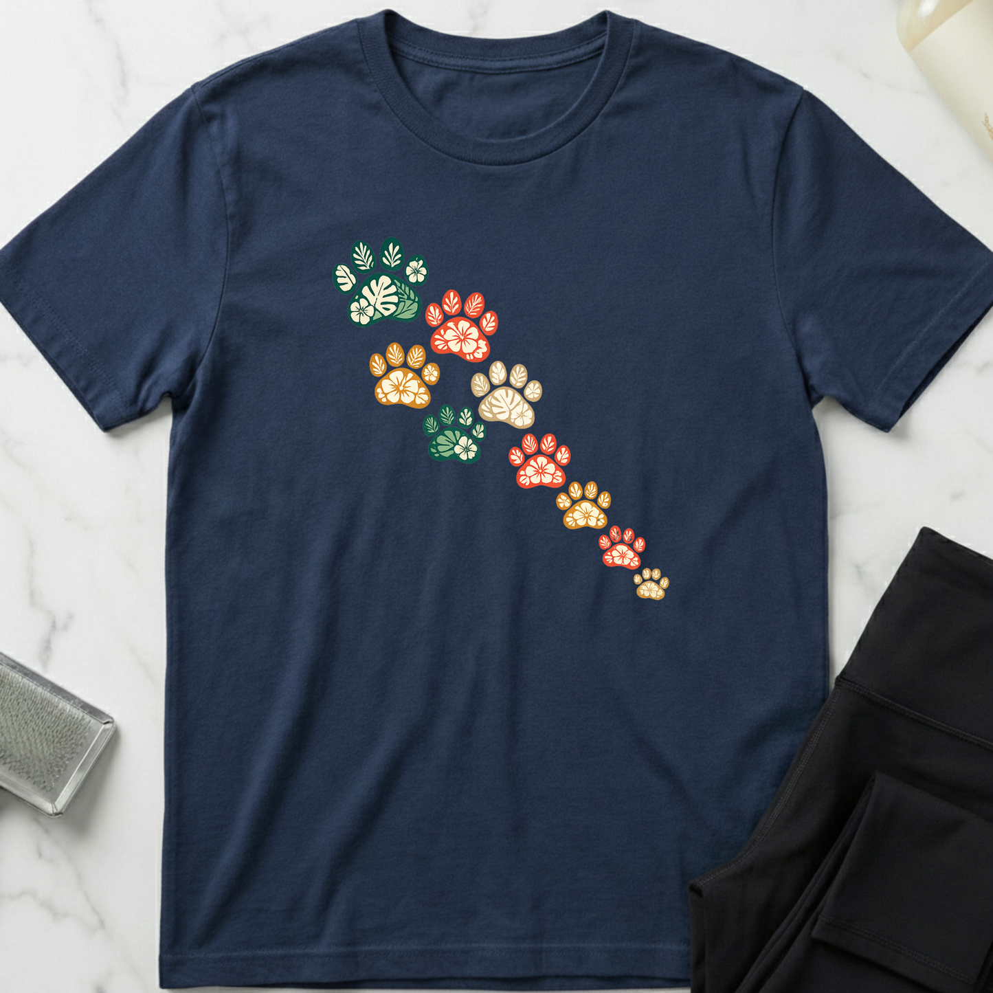 Navy blue t-shirt with colorful paw print design on a marble surface. Minimalist dog apparel by pemuyo.
