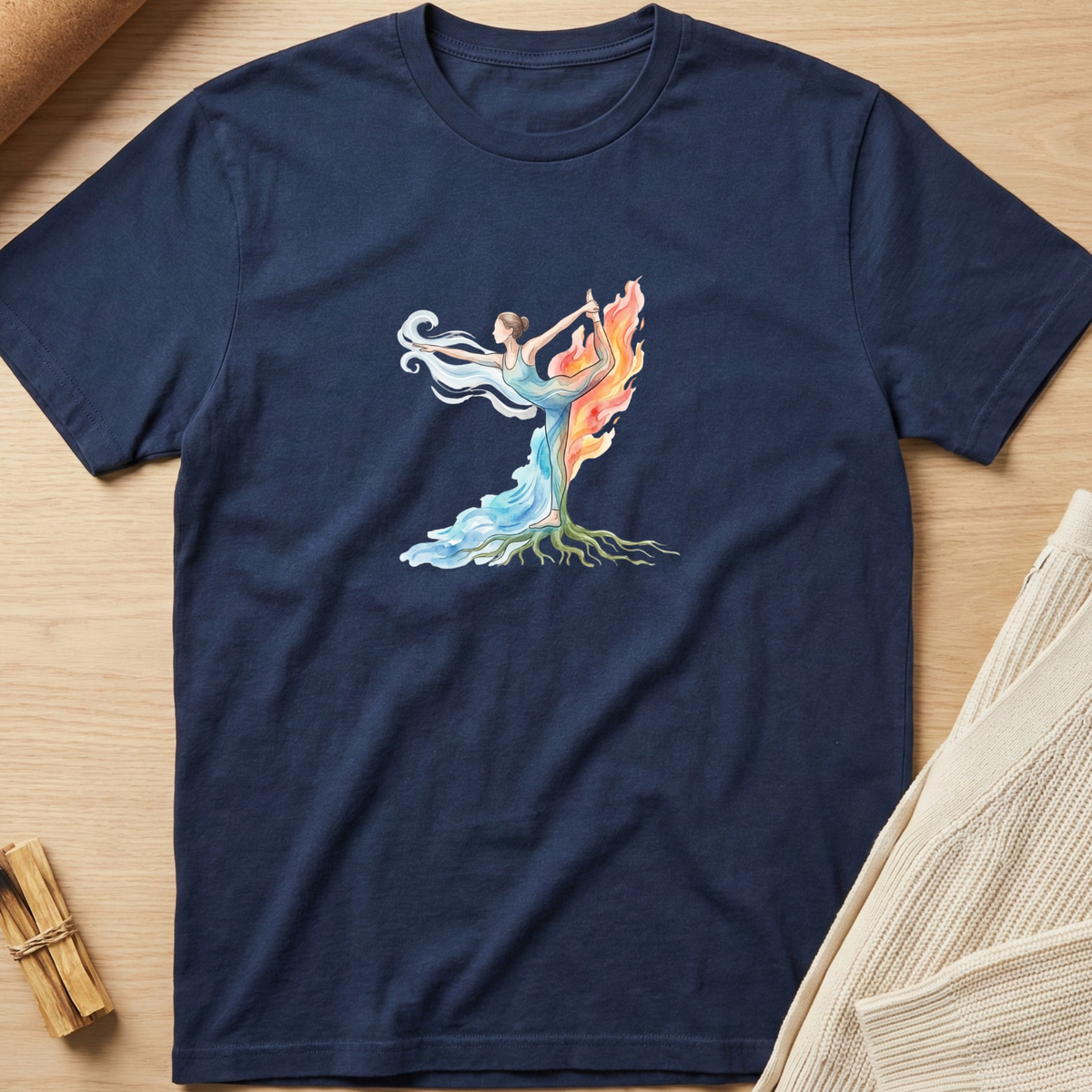 A navy blue short-sleeve t-shirt with a colorful graphic of a female dancer whose body forms a tree with flowing blue, orange, and green elements, laid flat on a light wood background. Minimalist yoga apparel by pemuyo.