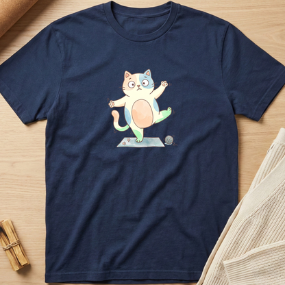 A navy blue short-sleeve t-shirt with a cartoon graphic of a round, belly-button-faced cat balancing on its hind legs. The shirt is displayed flat on a light wood background with neutral props. Minimalist yoga apparel by pemuyo.