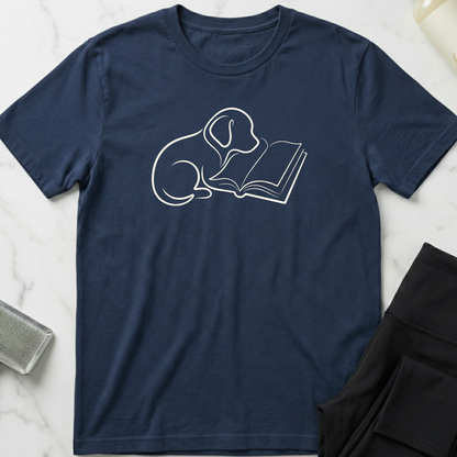 Navy blue t-shirt with a white dog reading a book graphic on a marble surface. Minimalist dog apparel by pemuyo.