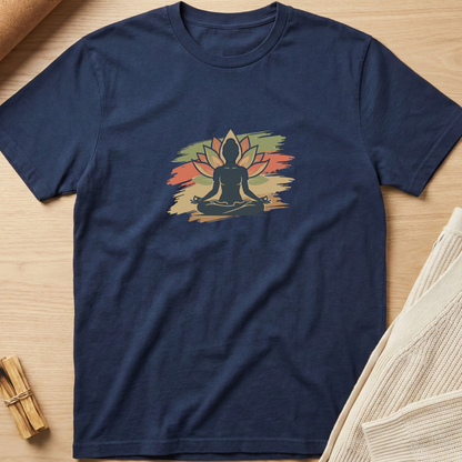 A navy blue short-sleeve t-shirt laid flat on a light wood surface, featuring a central graphic of a meditating silhouette in front of a lotus flower on a distressed multicolor background. Minimalist yoga apparel by pemuyo.