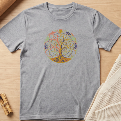 A heather gray short-sleeve t-shirt with a colorful circular tree of life graphic on the chest, laid flat on a light wood surface with neutral props. Minimalist yoga apparel by pemuyo.