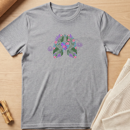 A heather gray short-sleeve crewneck t-shirt featuring a colorful butterfly graphic on the chest with green leaves, pink flowers, and purple accents, laid flat on a light wood background. Minimalist yoga apparel by pemuyo.