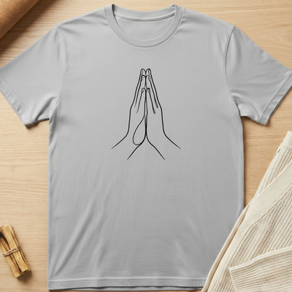 Gray t-shirt with a black line drawing of praying hands on a wooden surface. Minimalist yoga apparel by pemuyo.