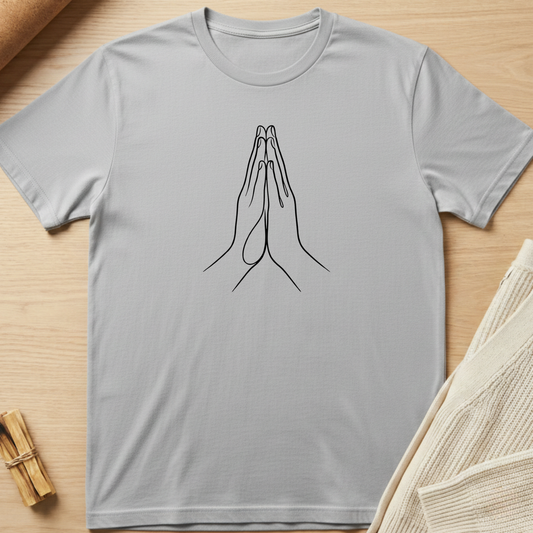 Gray t-shirt with a black line drawing of praying hands on a wooden surface. Minimalist yoga apparel by pemuyo.