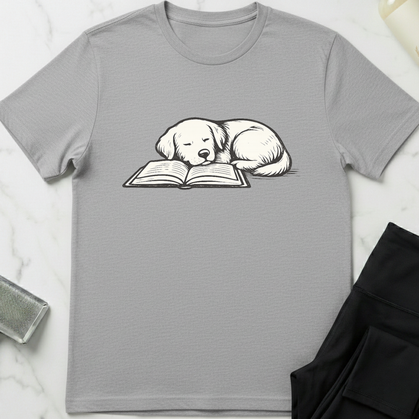 Gray t-shirt with a dog reading a book graphic on a white marble surface. Minimalist dog apparel by pemuyo.