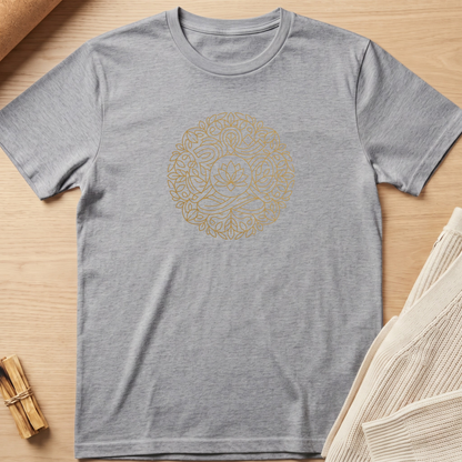 A heather gray short-sleeve t-shirt with a circular gold mandala-style graphic printed on the chest, laid flat on a light wood background with styled props. Minimalist yoga apparel by pemuyo.