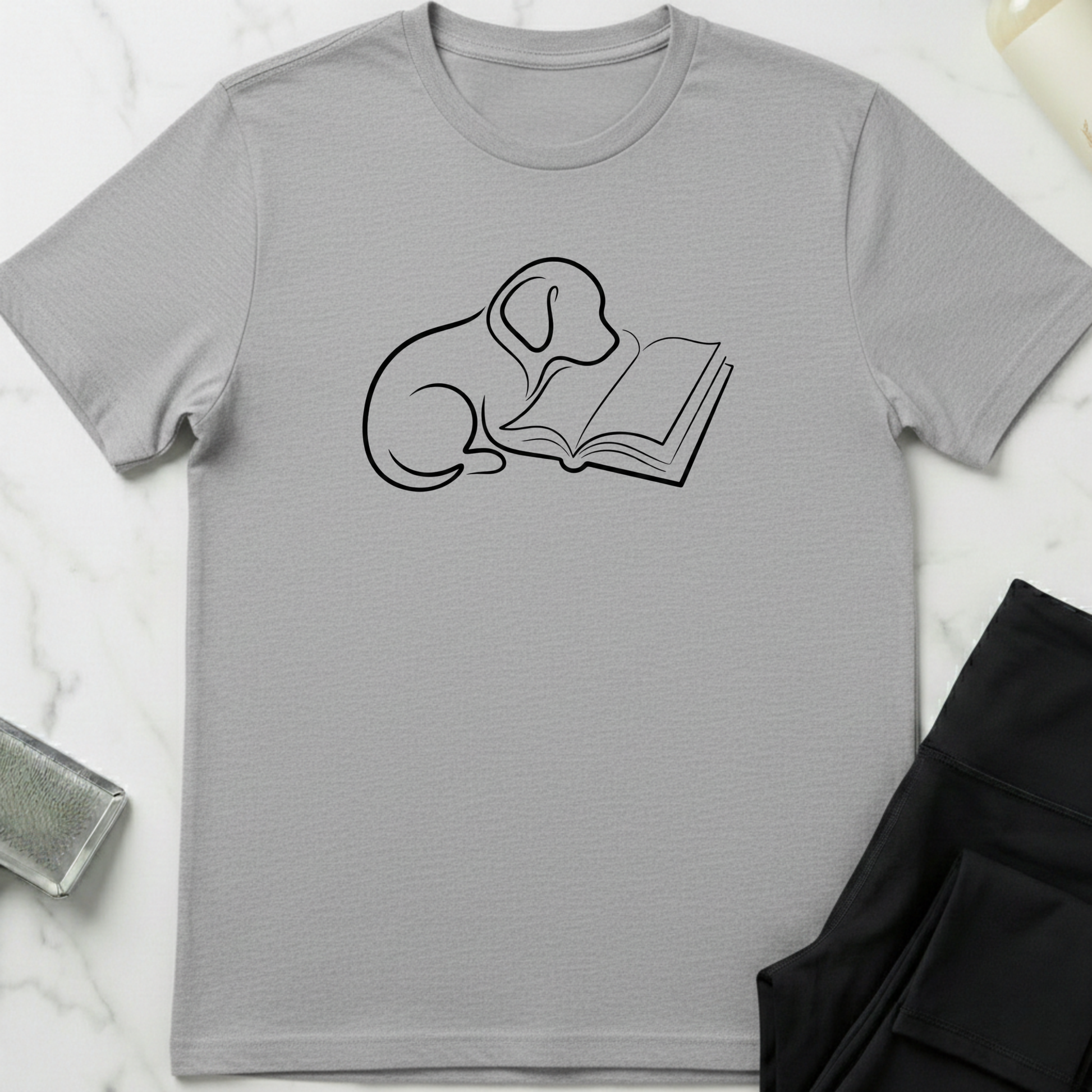 Gray t-shirt with a graphic of a dog and book a on a white marble surface. Minimalist dog apparel by pemuyo.