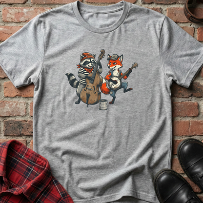 Gray t-shirt with cartoon raccoon and fox playing instruments on a brick background. Minimalist music apparel by pemuyo.