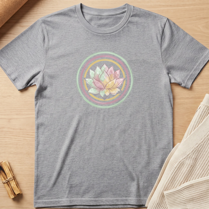 A heather gray short-sleeve t-shirt with a pastel lotus flower graphic inside concentric circles on the chest, laid flat on a light wood surface with neutral props. Minimalist yoga apparel by pemuyo.