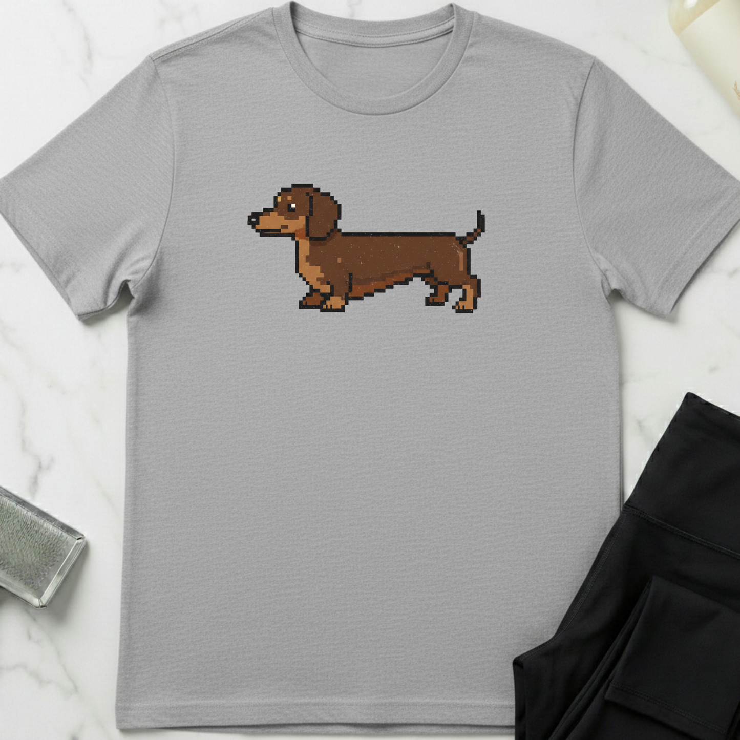 Gray t-shirt with a pixelated dachshund graphic on a marble surface. Minimalist dog apparel by pemuyo.