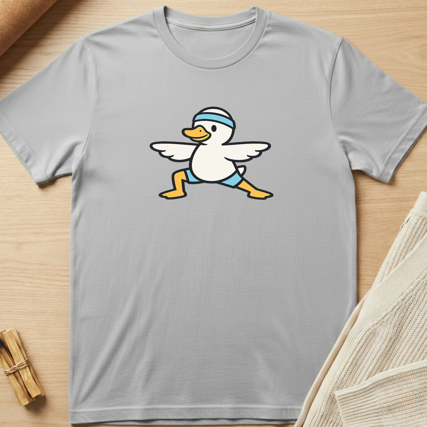 Gray t-shirt with a cartoon duck design on a wooden surface. Minimalist yoga apparel by pemuyo.