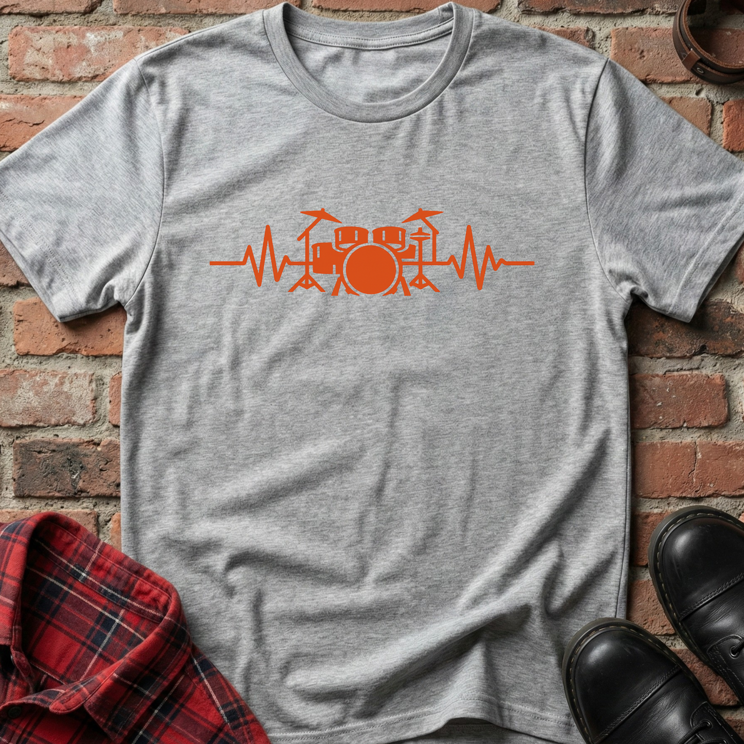 Gray t-shirt with orange drum set heartbeat design on a brick surface. Minimalist music apparel by pemuyo.