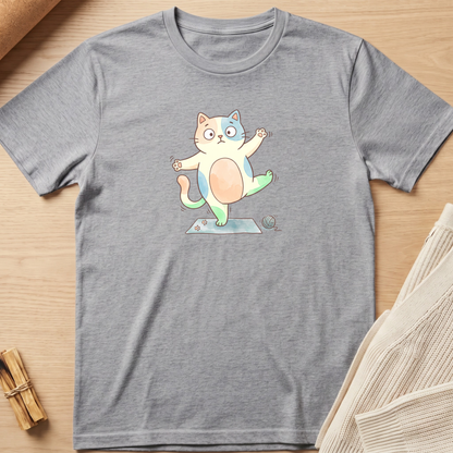 A heather gray short-sleeve t-shirt laid flat on a light wood surface, featuring a colorful cartoon cat graphic on the chest performing a yoga pose. Minimalist yoga apparel by pemuyo.