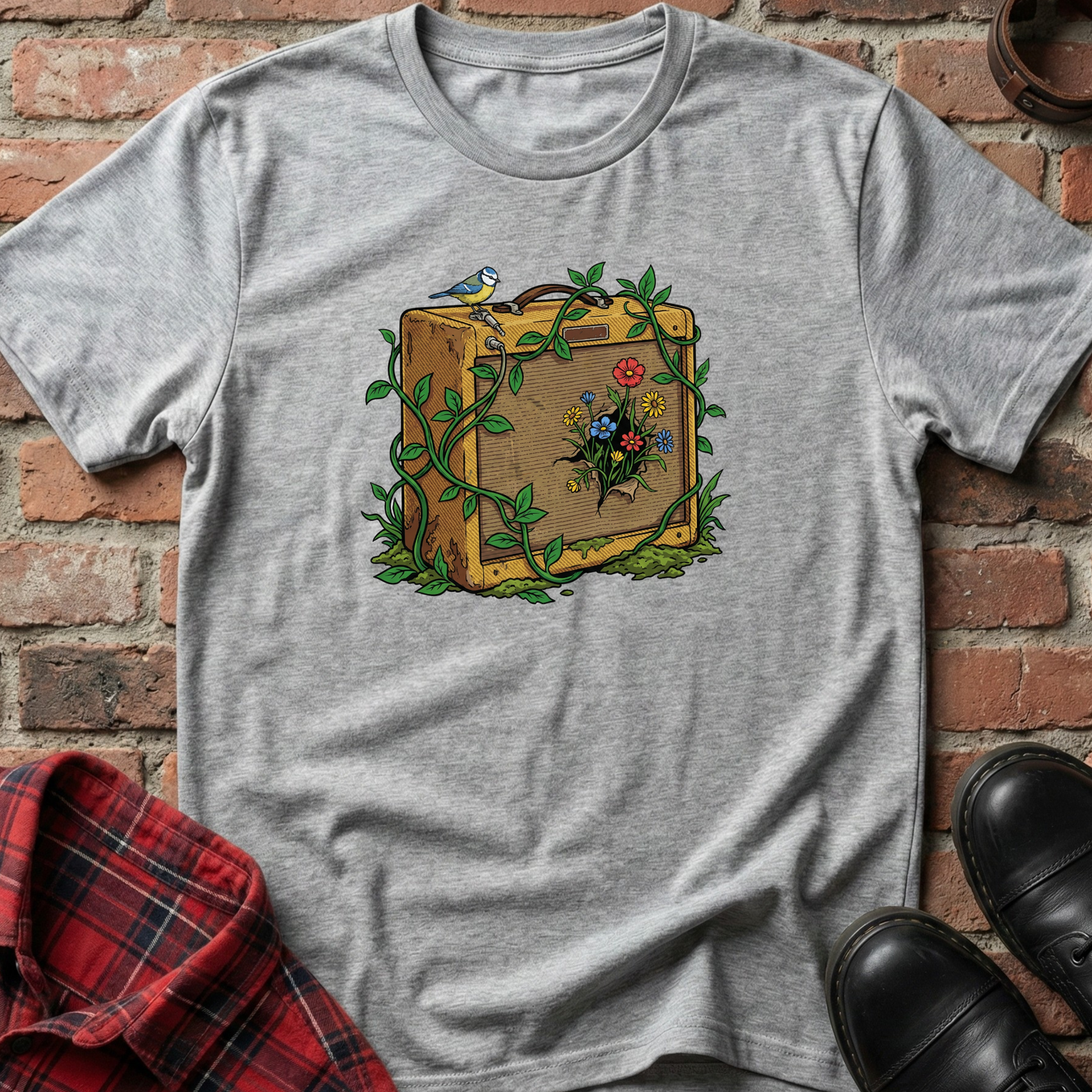 Gray t-shirt with a suitcase and nature-themed design on a brick surface. Minimalist music apparel by pemuyo.