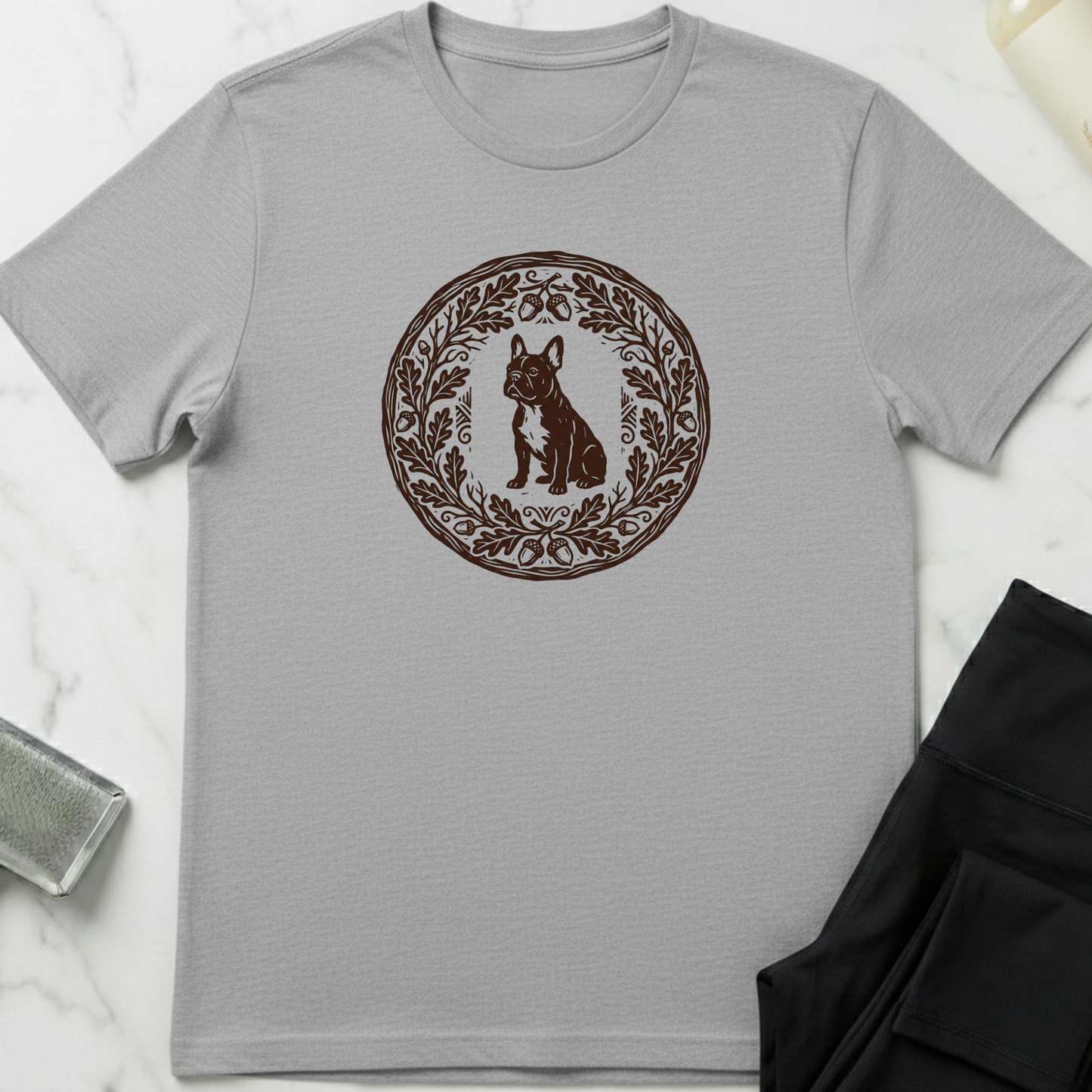 Gray t-shirt with a brown circular design featuring a dog and leaves on a white marble surface. Minimalist dog apparel by pemuyo.