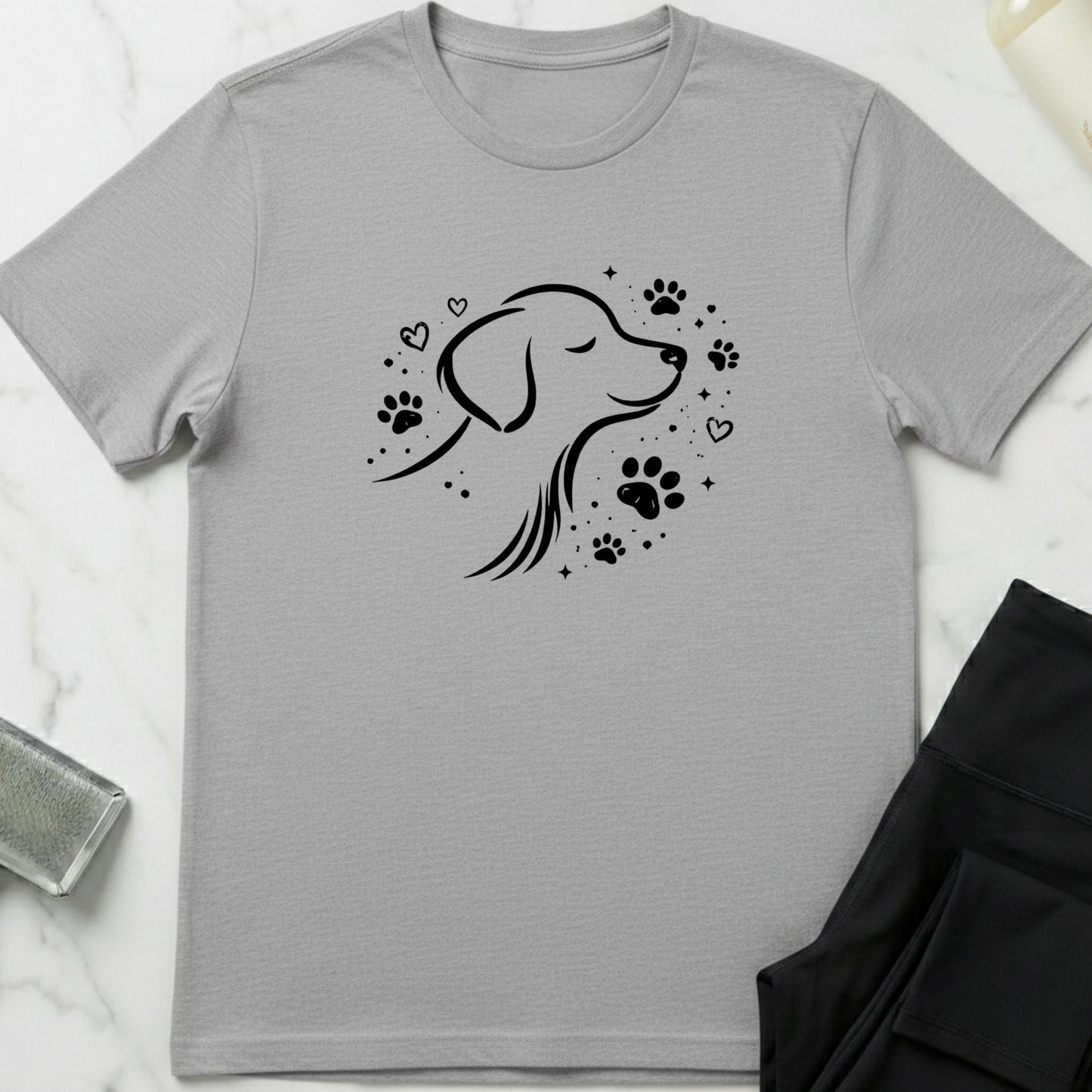 Gray t-shirt with a black dog illustration and paw prints on a white marble surface. Minimalist dog apparel by pemuyo.