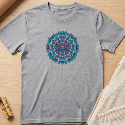 A heather gray short-sleeve crewneck t-shirt featuring a colorful mandala graphic in shades of blue, purple, and teal on the chest, laid flat on a light wood background with styled props. Minimalist yoga apparel by pemuyo.