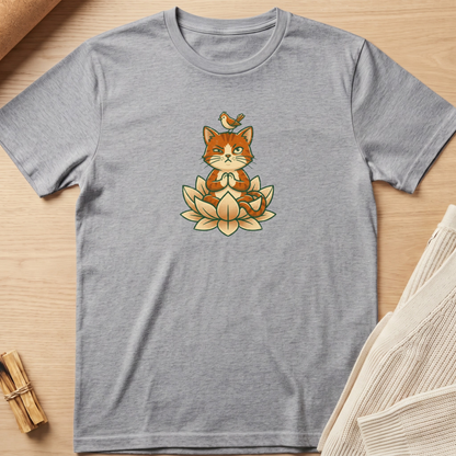 A heather gray short-sleeve t-shirt laid flat on a light wood surface, featuring a central graphic of an orange cat meditating on a lotus flower with a small bird on its head. Minimalist yoga apparel by pemuyo.