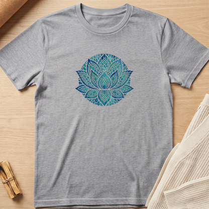 A heather gray short-sleeve t-shirt with a blue and green mandala lotus print on the chest, laid flat on a light wood background with styled props. Minimalist yoga apparel by pemuyo.