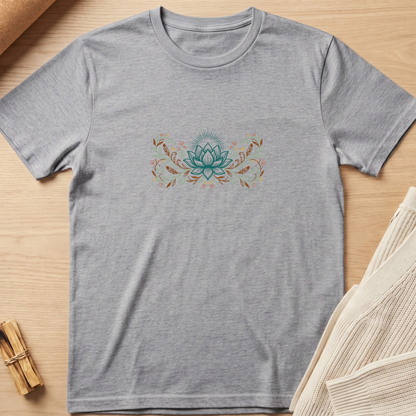 A heather gray short-sleeve t-shirt with a central teal and orange lotus flower graphic, laid flat on a light wood background with a knit fabric prop in the corner. Minimalist yoga apparel by pemuyo.