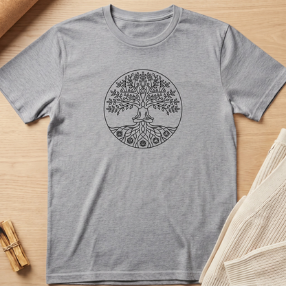 A heather gray short-sleeve t-shirt with a black circular tree of life graphic on the chest, laid flat on a light wood background with neutral props. Minimalist yoga apparel by pemuyo.