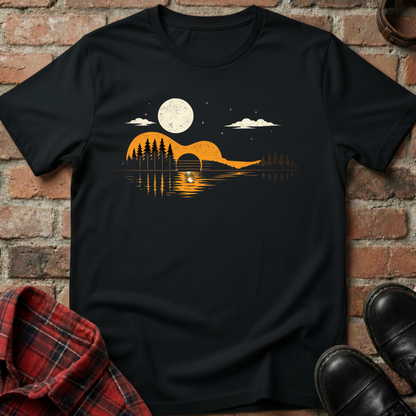 Black t-shirt with a nature graphic design featuring a moon, trees, and a lake, displayed against a brick wall. Minimalist music apparel by pemuyo.