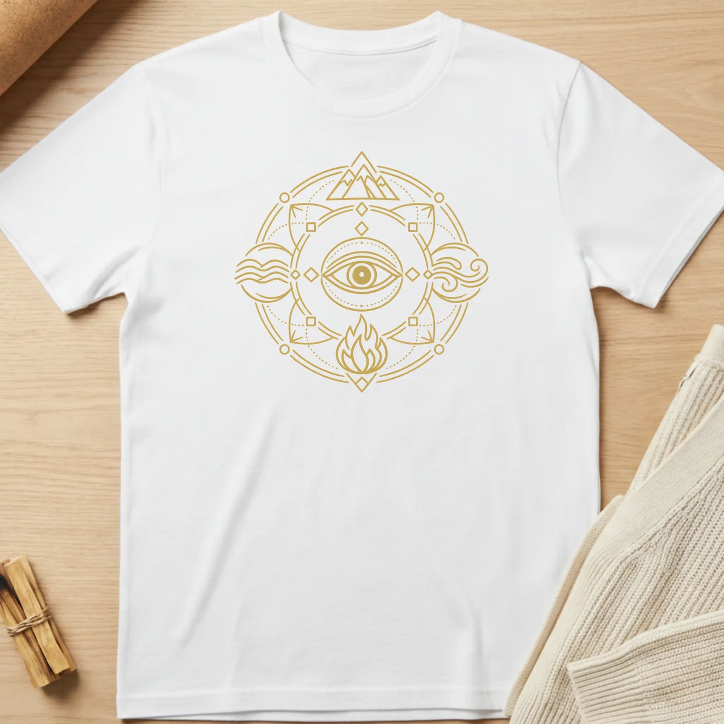 White t-shirt with gold geometric design featuring an eye and flame on a wooden surface. Minimalist yoga apparel by pemuyo.