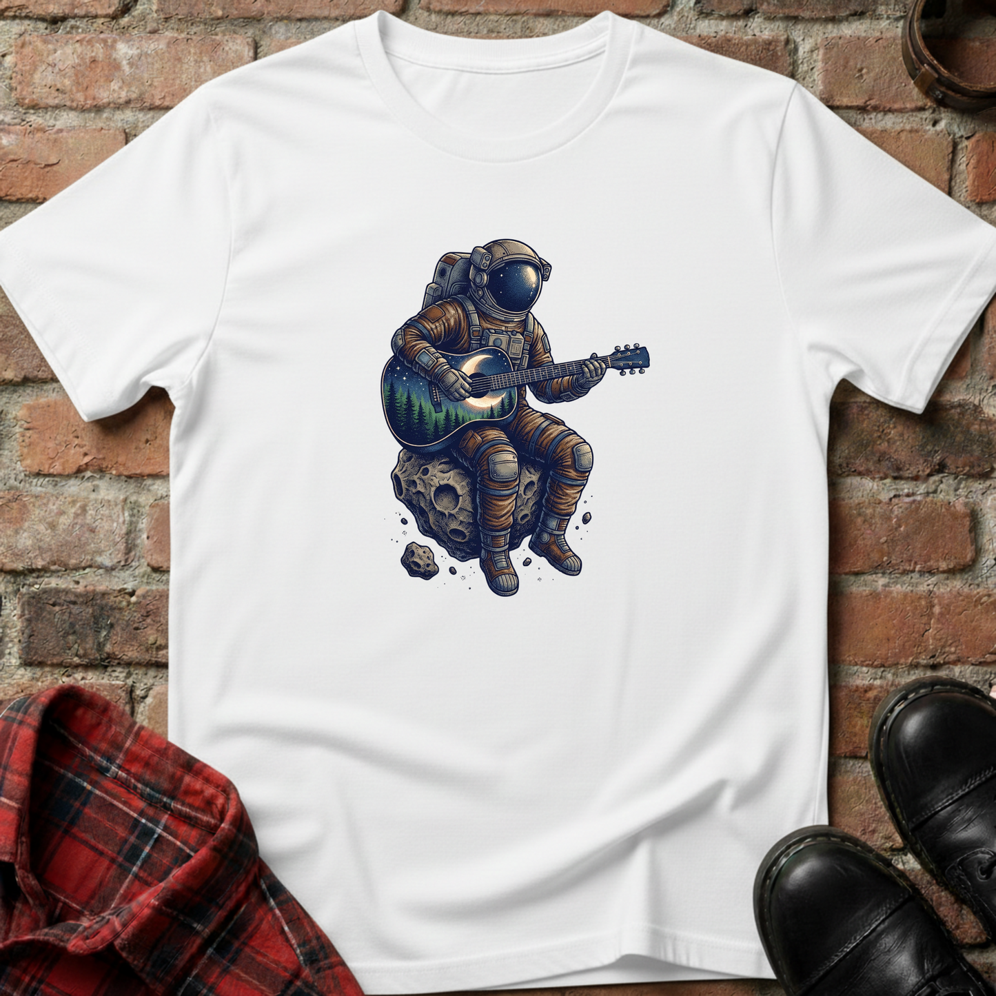 White t-shirt with an astronaut playing guitar on a rock design, placed against a brick wall. Minimalist music apparel by pemuyo.
