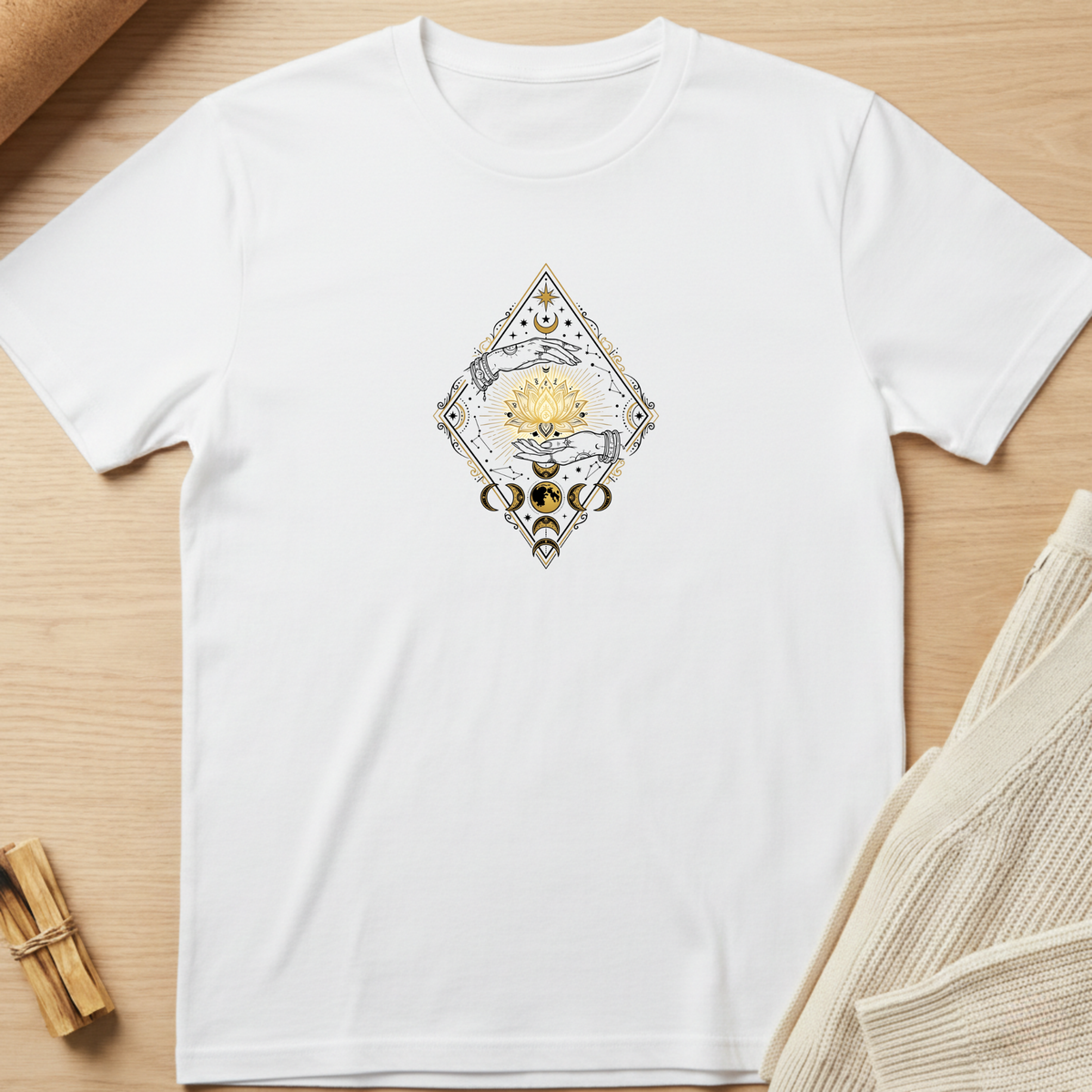 A white short-sleeve crewneck t-shirt laid flat on a light wood background, featuring a central graphic of a diamond-shaped design with a yellow sun and blue hands. Minimalist yoga apparel by pemuyo.