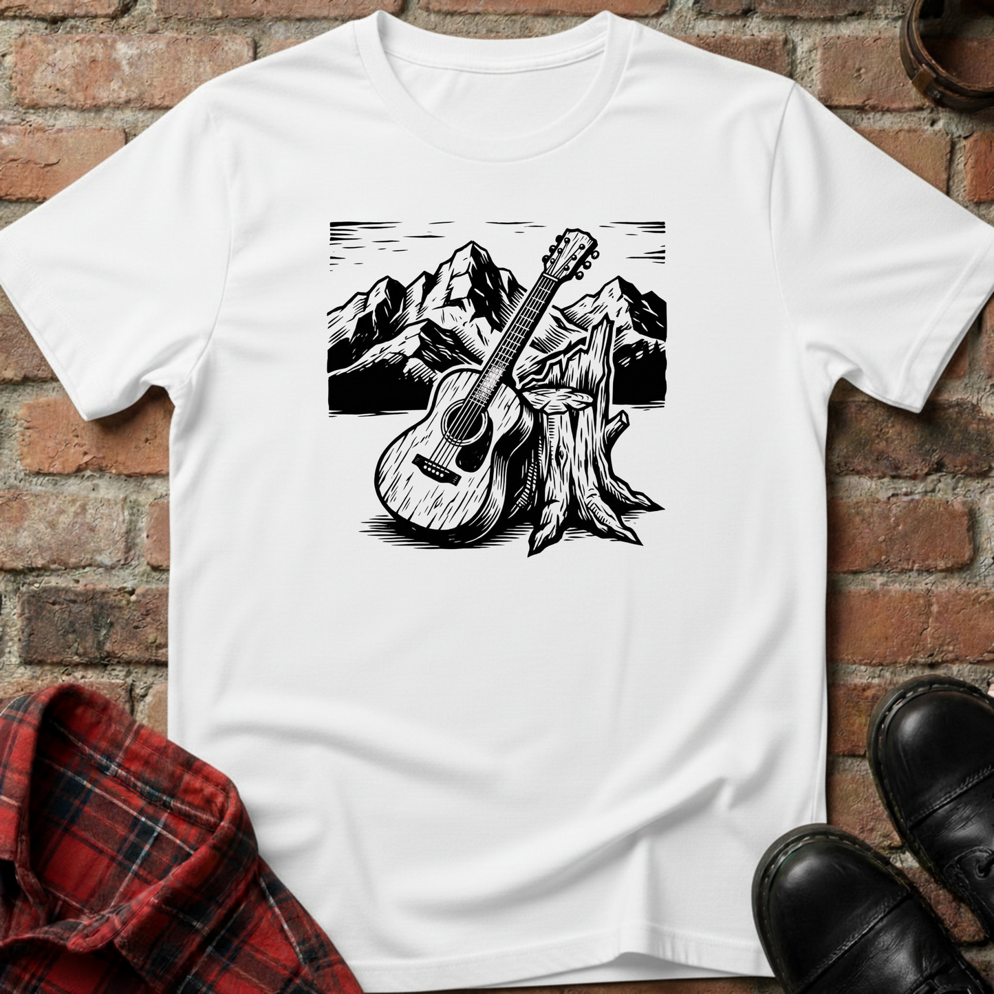 White t-shirt with a black and white graphic of a guitar leaning against a tree stump with mountains in the background, placed on a brick surface. Minimalist music apparel by pemuyo.