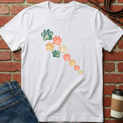White t-shirt with colorful paw prints on a brick wall background. Minimalist dog apparel by pemuyo.