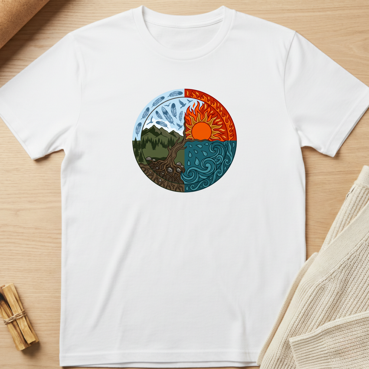 A white short-sleeve crewneck t-shirt laid flat on a light wood surface, featuring a circular graphic of a yin-yang style nature design with a mountain, tree, sun, and wind motifs in blue, orange, green, and brown. Minimalist yoga apparel by pemuyo.