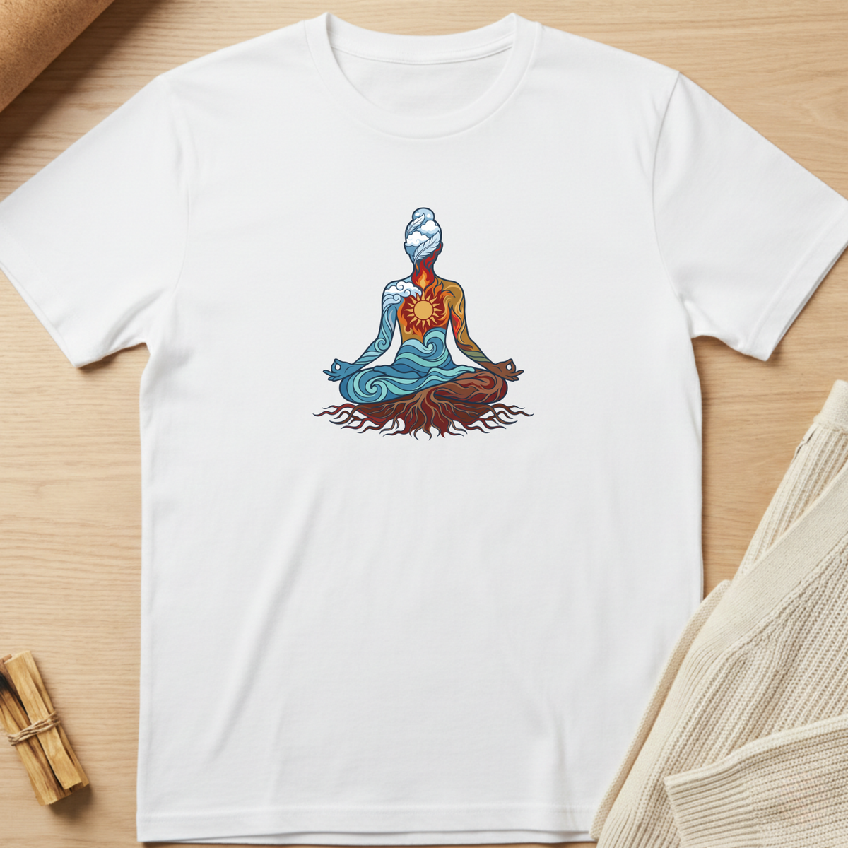 A white short-sleeve crewneck t-shirt laid flat on a light wood surface, featuring a colorful graphic of a meditating figure with blue, orange, and brown tones. Minimalist yoga apparel by pemuyo.