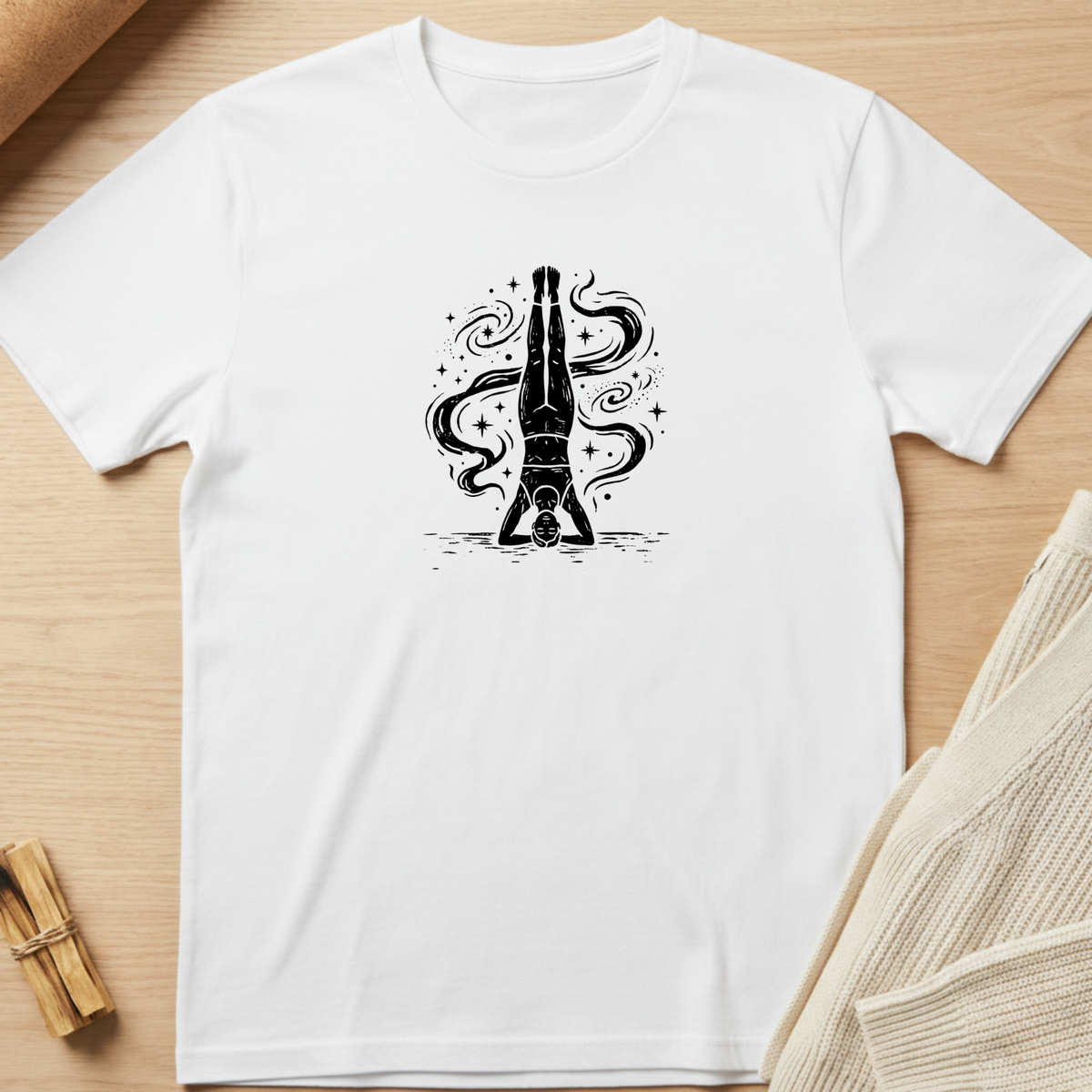 A white short-sleeve crewneck t-shirt laid flat on a light wood background, featuring a black graphic of a champagne bottle with swirling liquid details on the chest. Minimalist yoga apparel by pemuyo.