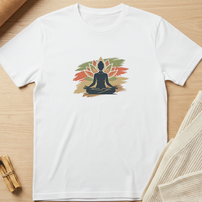 A white short-sleeve crewneck t-shirt laid flat on a light wood surface, featuring a central graphic of a seated meditating figure in black silhouette with a lotus flower in orange, red, and green brushstroke-style colors. Minimalist yoga apparel by pemuyo.
