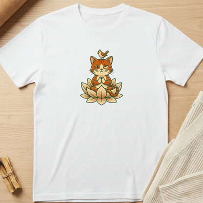 A white short-sleeve crewneck t-shirt laid flat on a light wood surface, featuring a central graphic of a cute orange cat meditating on a lotus flower with a small bird on its head. Minimalist yoga apparel by pemuyo.