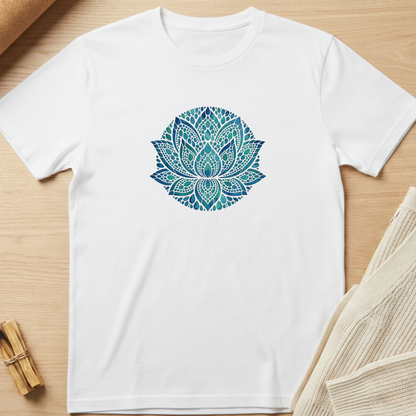A white short-sleeve crewneck t-shirt featuring a circular mandala lotus design in shades of teal and blue on the chest, laid flat on a light wood background with neutral props. Minimalist yoga apparel by pemuyo.
