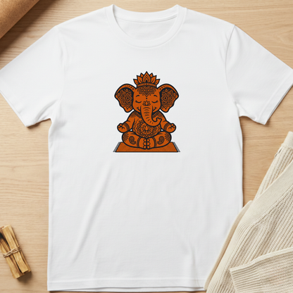 A white short-sleeve crewneck t-shirt featuring a central graphic of Ganesha in orange and brown tones, laid flat on a light wood background with styled props. Minimalist yoga apparel by pemuyo.
