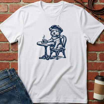 White t-shirt with a dog illustration sitting at a table and drinking coffee, placed against a brick wall. Minimalist dog apparel by pemuyo.
