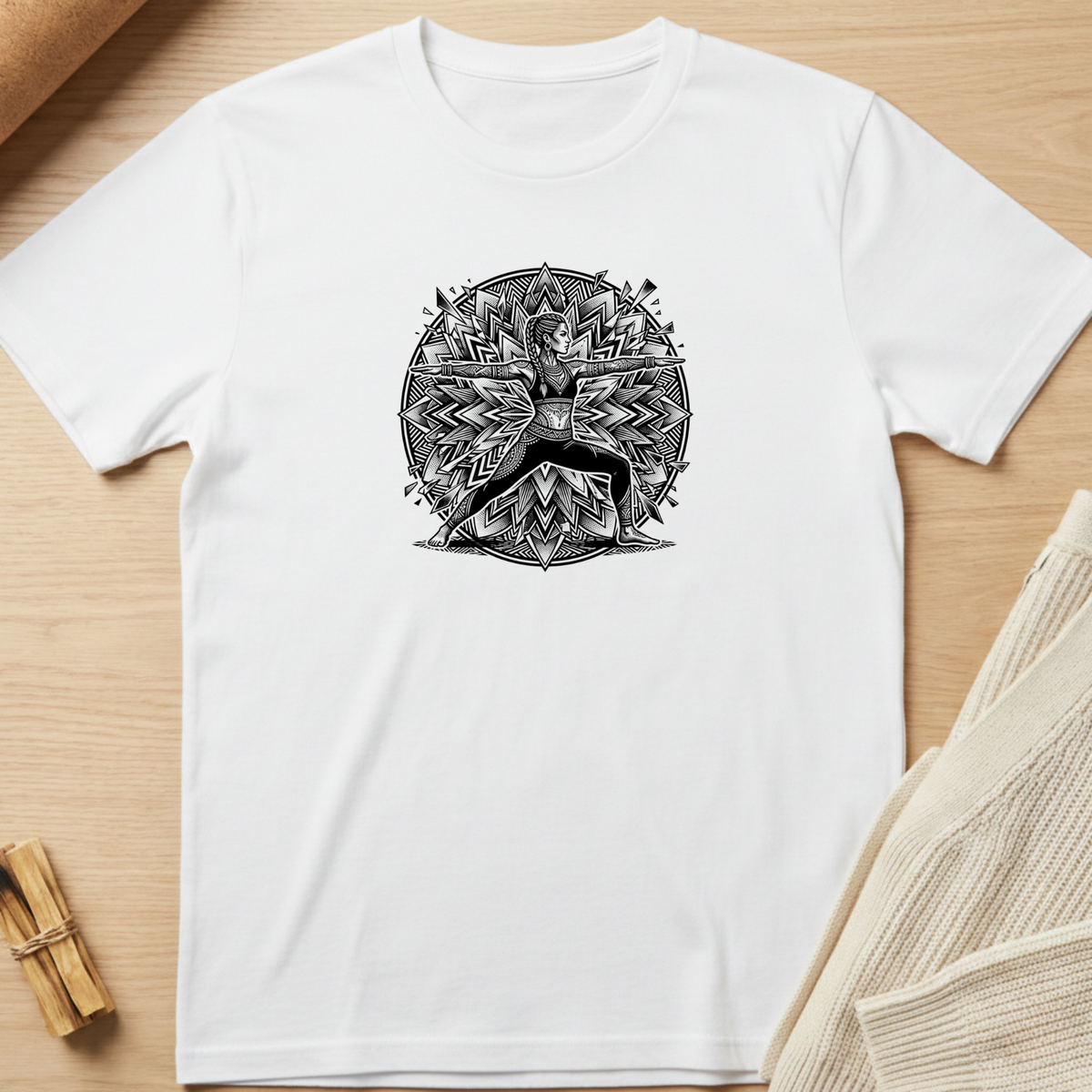 A white short-sleeve crewneck t-shirt with a black circular mandala-style graphic of a deer in the center, laid flat on a light wood background with styled props. Minimalist yoga apparel by pemuyo.