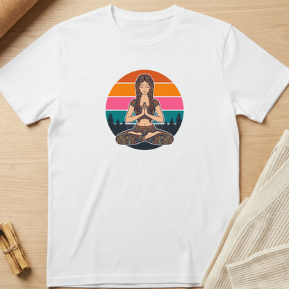 A white short-sleeve crewneck t-shirt laid flat on a light wood surface, featuring a colorful graphic of a woman meditating in front of a sunset circle. Minimalist yoga apparel by pemuyo.